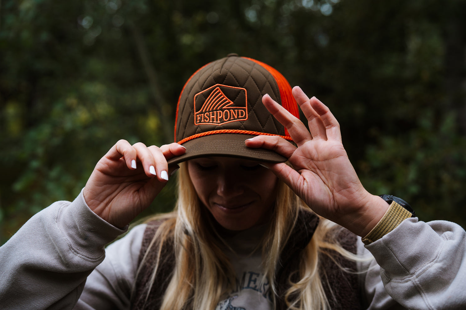 Person wearing a brown and orange cap with 'Fishpond' logo in a forest setting