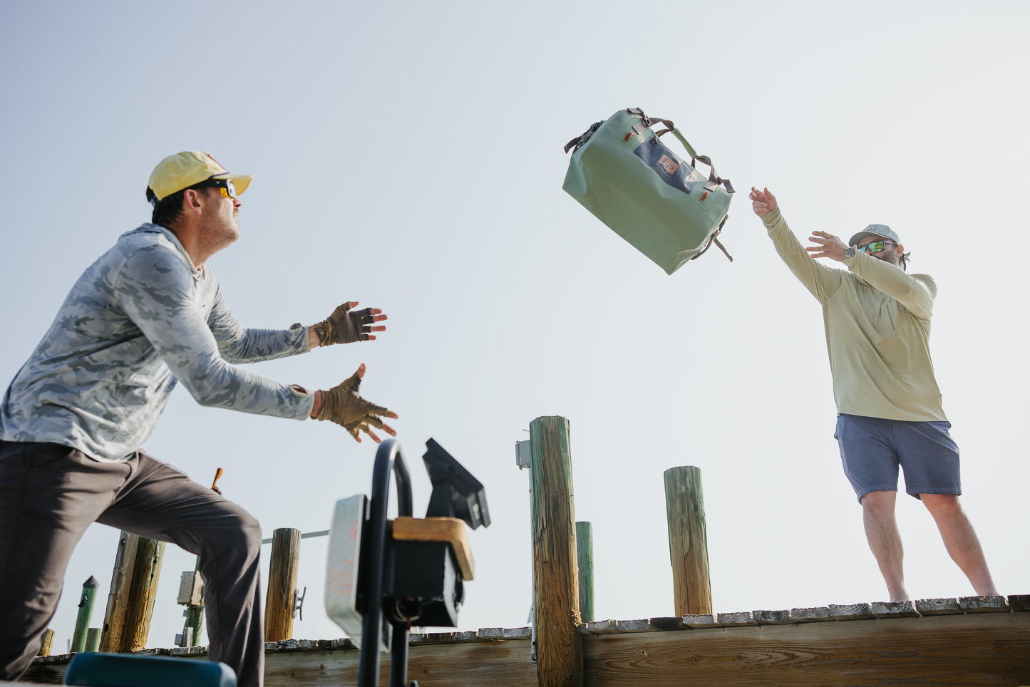 Two people on a wooden platform with one person throwing a green bag into the air.